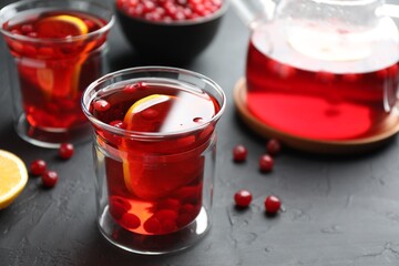 Tasty hot cranberry tea with lemon and fresh berries in glass on black textured table