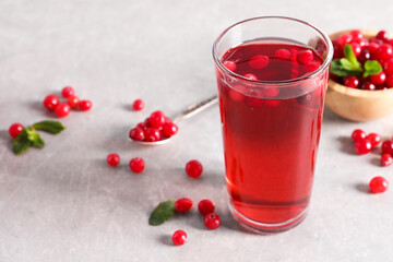 Tasty cranberry juice in glass and fresh berries on light grey table
