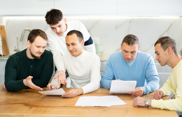 Troubled man reading legal notice surrounded by friends providing moral support sitting at table n...