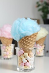 Sweet cotton candies in waffle cones and marshmallows on white table indoors, closeup