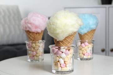Sweet cotton candies in waffle cones and marshmallows on white table indoors, closeup