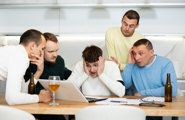 Fototapeta premium Men drink beer and try to help friend solve problems using laptop and the Internet