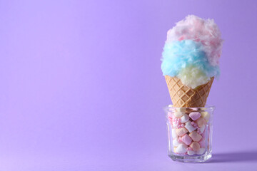 Sweet cotton candy in waffle cone on purple background, closeup. Space for text
