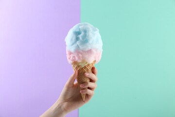 Woman holding waffle cone with cotton candy on color background, closeup