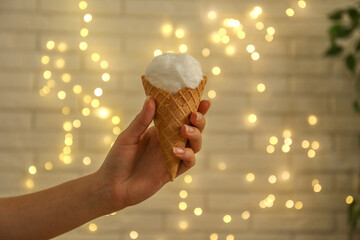 Woman holding waffle cone with cotton candy against blurred lights, closeup