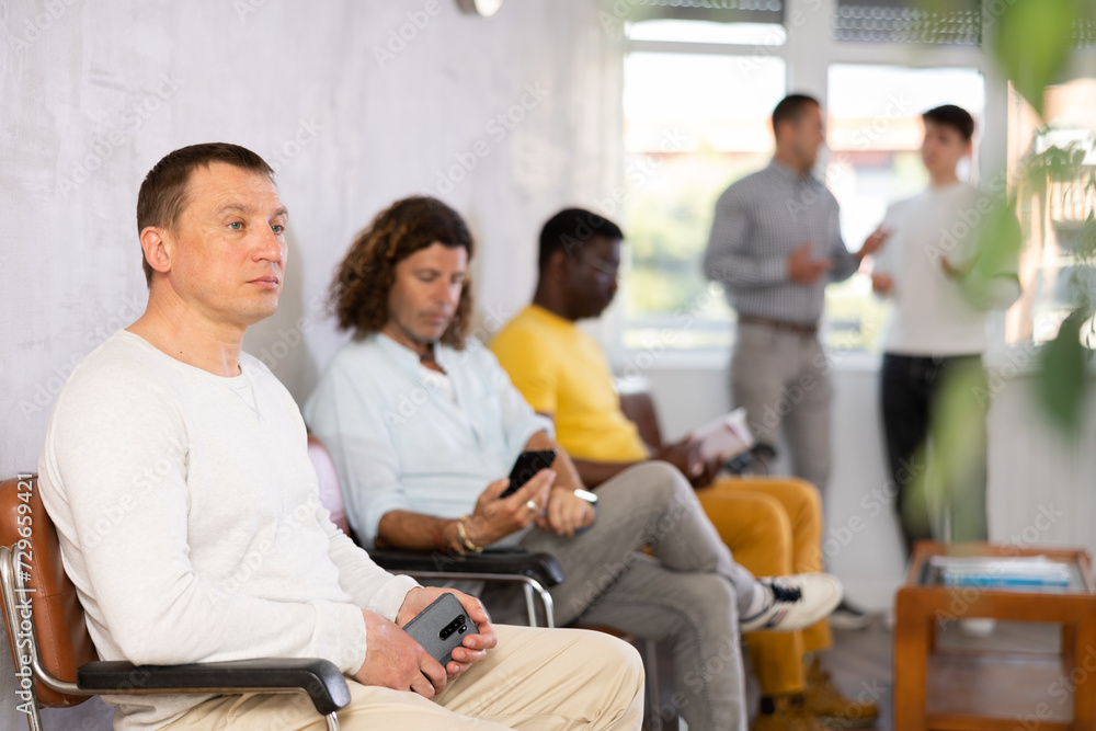 Wall mural portrait of a focused european man sitting in a chair in the lobby waiting