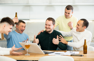 Fototapeta premium Group of football fans drinking beer and watching football match on a laptop at home
