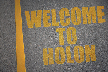 asphalt road with text welcome to Holon near yellow line.