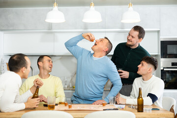 Friends drinking beer and enthusiastically playing a board game at home
