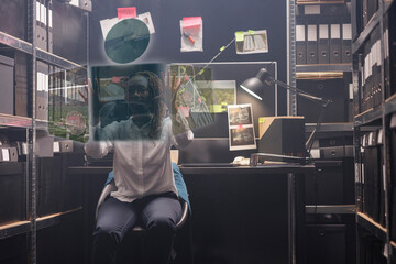Young policewoman looking at clues in hologram, examining augmented reality holographic photos to solve felony in police archive room. Private detective working with artificial intelligence. - obrazy, fototapety, plakaty