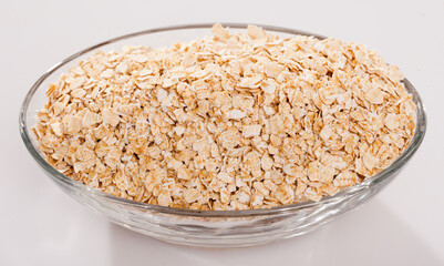 Oat flakes in oval glass bowl on white surface. Concept of healthy food..