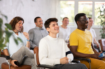 Group of positive men of different nationalities listening to a lecture in the lobby dedicated to...