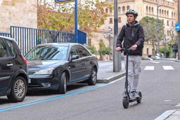 Young caucasian guy riding an electric scooter, on the road, with a helmet and a backpack, in the city.
