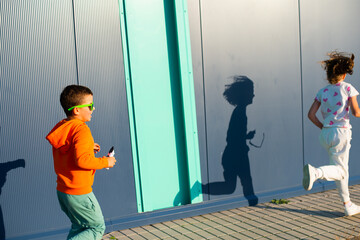 Cheerful smiling children, boy and girl 7 and 8 years old in bright sunglasses playing tag on the street	 - 729673088