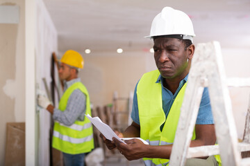 African-american foreman with documents, analyzing plan of renovation works in apartment.