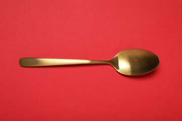 One shiny golden spoon on red background, top view
