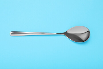 One shiny silver spoon on light blue background, top view
