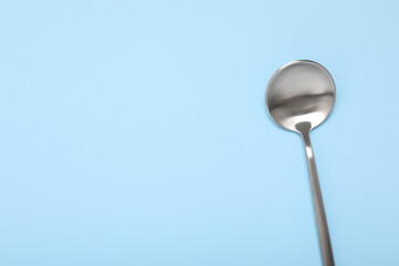 One shiny silver spoon on light blue background, top view. Space for text