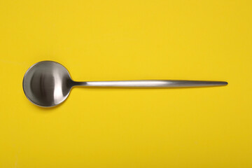 One shiny silver spoon on yellow background, top view