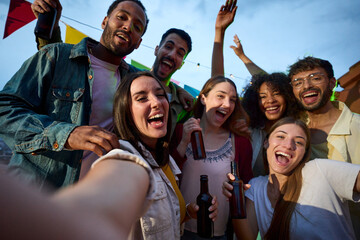 Cheerful attractive young woman taking selfie at millennial alcohol party surrounded by group happy...
