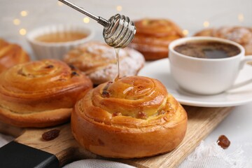 Pouring honey onto delicious rolls with raisins at table, closeup. Sweet buns