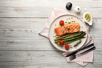 Tasty grilled salmon with tomatoes, asparagus and spices served on wooden table, flat lay. Space...