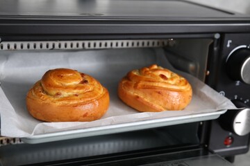 Delicious rolls with raisins on baking tray in oven. Cooking sweet buns