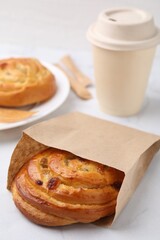 Delicious roll with raisins in paper bag on white table, closeup. Sweet bun