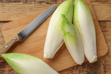 Fresh raw Belgian endives (chicory), board and knife on wooden table, top view