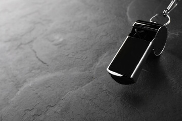 Referee equipment. Metal whistle on black textured background, closeup and space for text