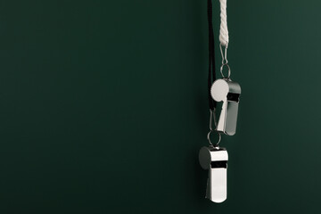 Referee equipment. Metal whistles on dark green background, closeup and space for text