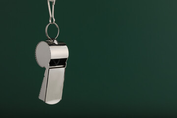 Referee equipment. Metal whistle on dark green background, closeup and space for text