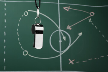Referee whistle against green chalkboard with game scheme, closeup. Space for text