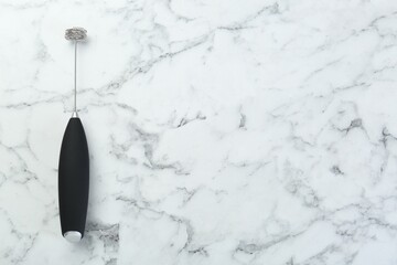 Black milk frother wand on white marble table, top view. Space for text