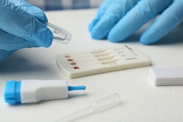 Doctor dropping buffer solution onto disposable multi-infection express test cassette at white...