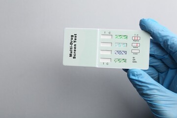 Doctor holding multi-drug screen test on light grey background, top view