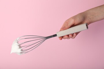 Woman holding whisk with whipped cream on pink background, closeup