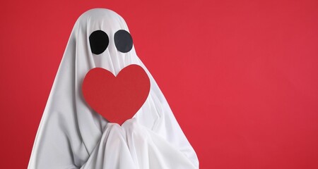 Cute ghost. Person covered with white sheet holding heart on red background, space for text