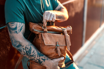 Close up of a tattooed guy's hand opening a rucksack on a street. - obrazy, fototapety, plakaty