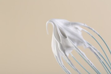 Whisk with whipped cream on beige background, closeup. Space for text