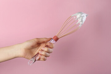 Woman holding whisk with whipped cream on pink background, closeup