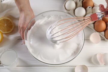 Woman making whipped cream with whisk at white wooden table, above view