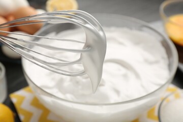 Whisk with whipped cream over bowl, closeup