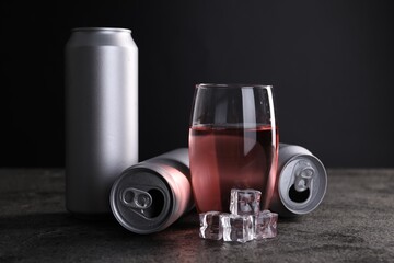 Energy drink in glass, aluminium cans and ice cubes on grey table