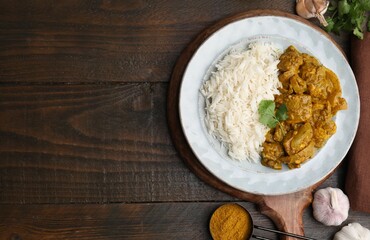Delicious chicken curry with rice and ingredients on wooden table, flat lay. Space for text