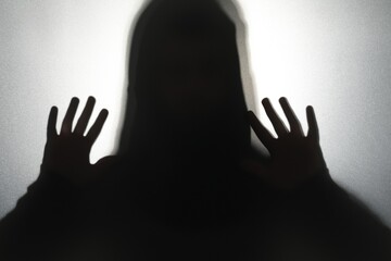 Silhouette of ghost behind glass against grey background