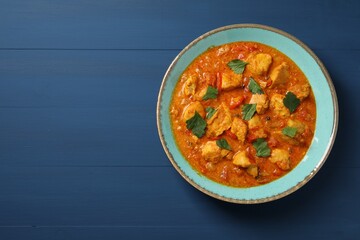 Delicious chicken curry on blue wooden table, top view. Space for text