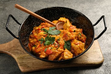 Delicious chicken curry in frying pan and spoon on grey table