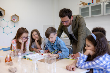 Obraz na płótnie Canvas Man teacher with kids during chemistry lesson in school classroom.