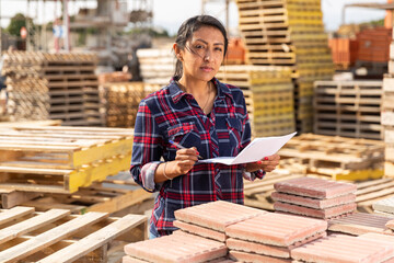Woman manager keeps records of building materials in the open area of a construction store